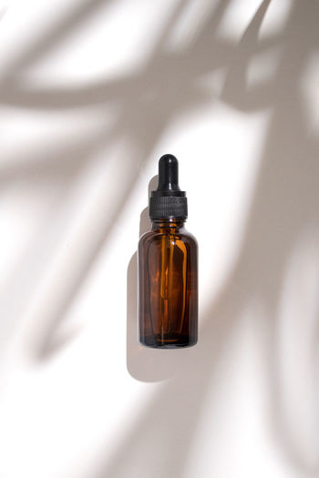 Amber glass dropper bottle with shadow leaves on white background. hyaluronic acid oil, serum 