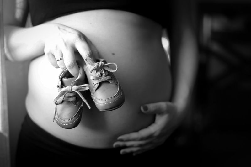 Midsection of pregnant woman holding shoes at home