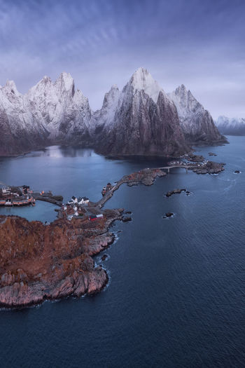 Residential houses located on islands near rough rocky mountains covered with snow against gloomy sky on cold winter day in norway