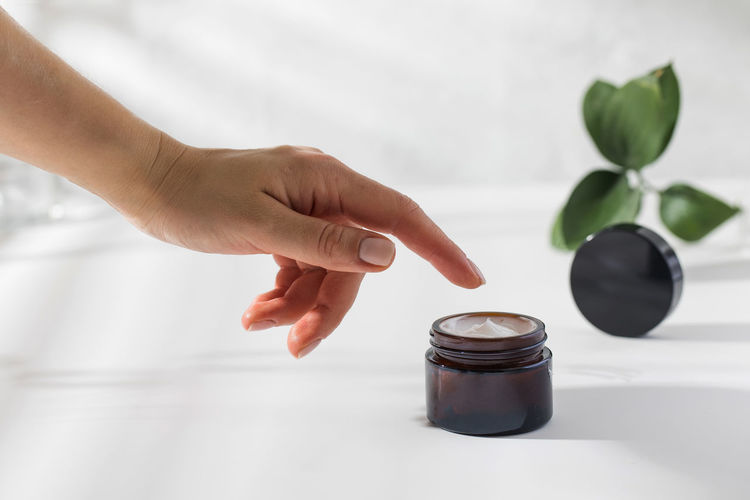 A woman's hand reaches for a jar of nourishing skin cream on a white background 