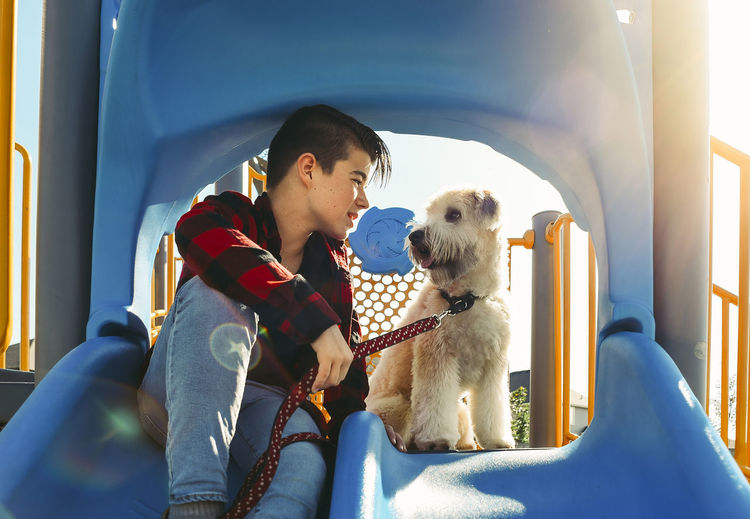 Boy looking at schnauzer while sitting on slide at playground during sunny day