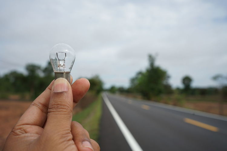 Cropped hand holding light bulb against sky