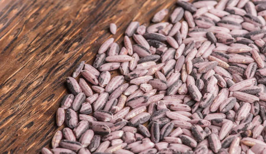 Raw red rice on a dark wooden plate, top view.