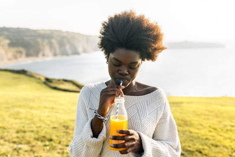 Young woman drinking orange juice at the coast