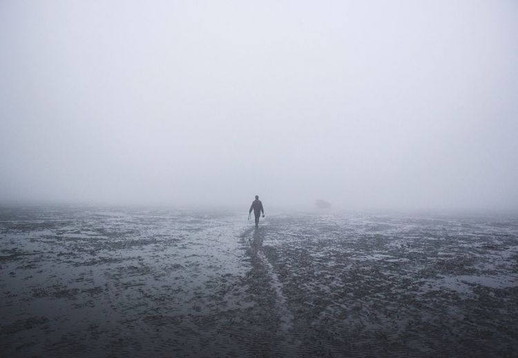 Silhouette man walking at beach against clear sky during foggy weather