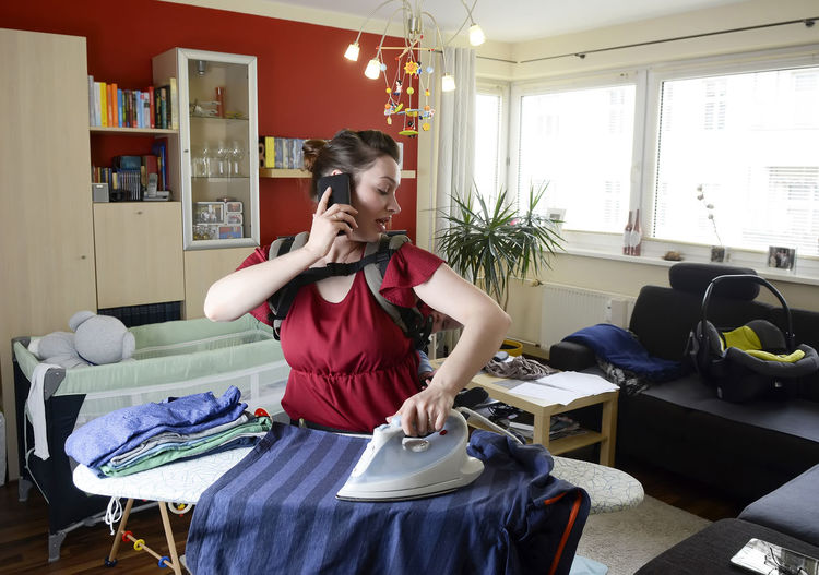 Young woman ironing clothing while talking over phone at home