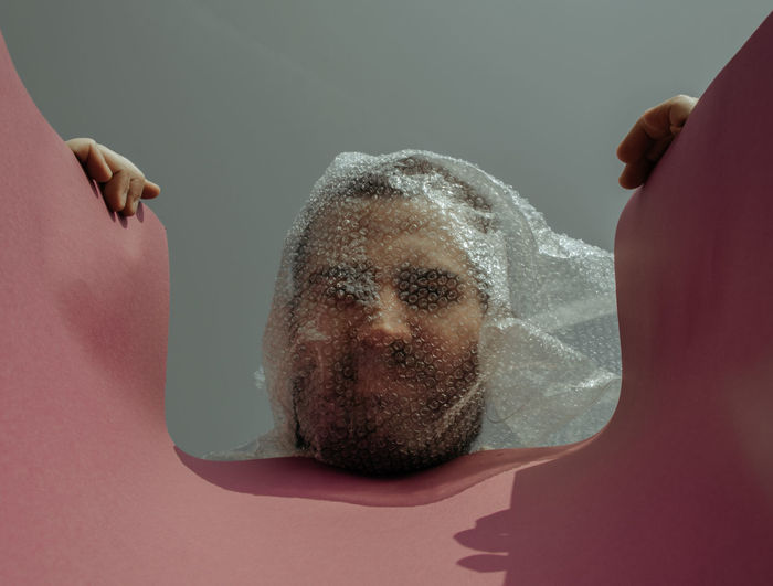 Man with face covered by bubble wrap against clear sky