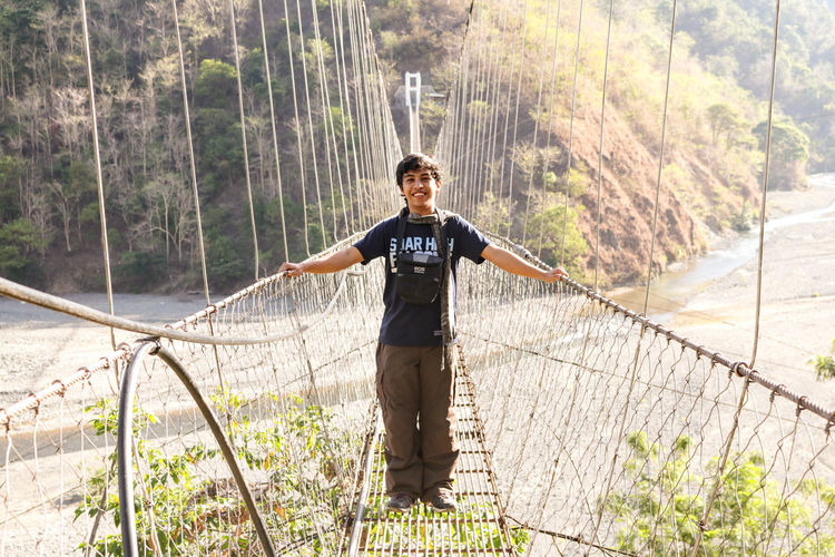 Portrait of smiling young man on footbridge over river at mount pulag