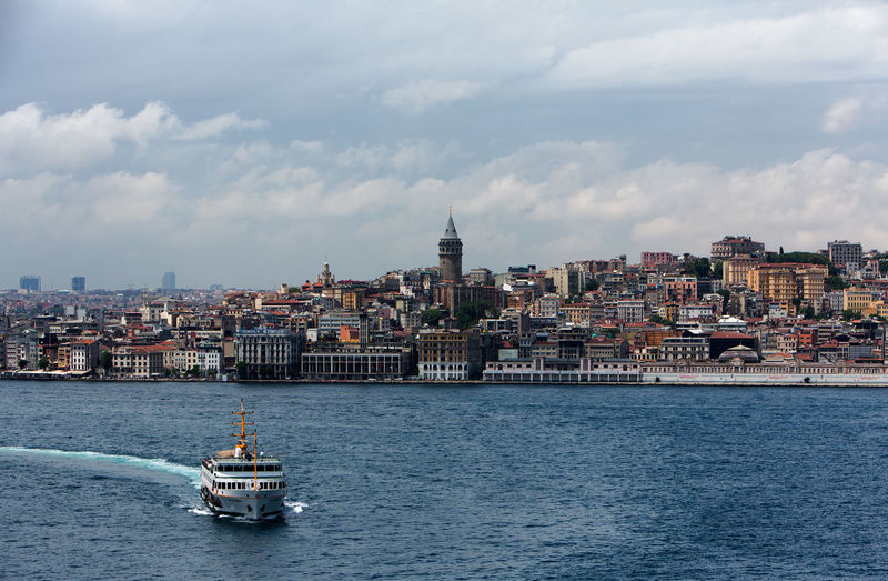 High angle view of ship sailing on strait by buildings against cloudy sky