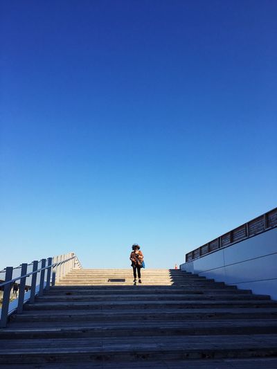 Low angle view of woman walking on steps against clear sky