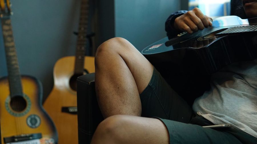 Midsection of man playing guitar while sitting at home