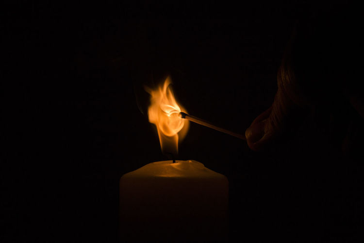 Cropped image of person igniting candle in darkroom