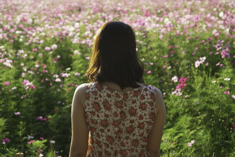 Rear view of woman standing against flowering plants
