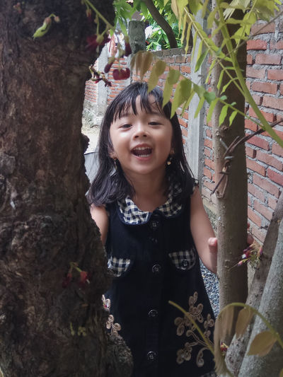 Close-up of smiling girl standing against tree trunk