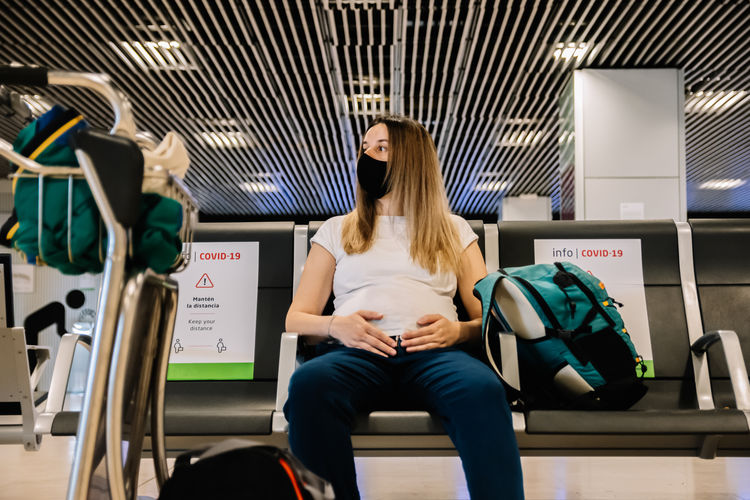 Pregnant woman with face mask sitting while waiting for her flight departure at the airport. 