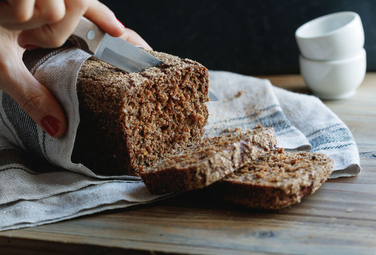 Cropped hand of woman cutting brown bread from knife