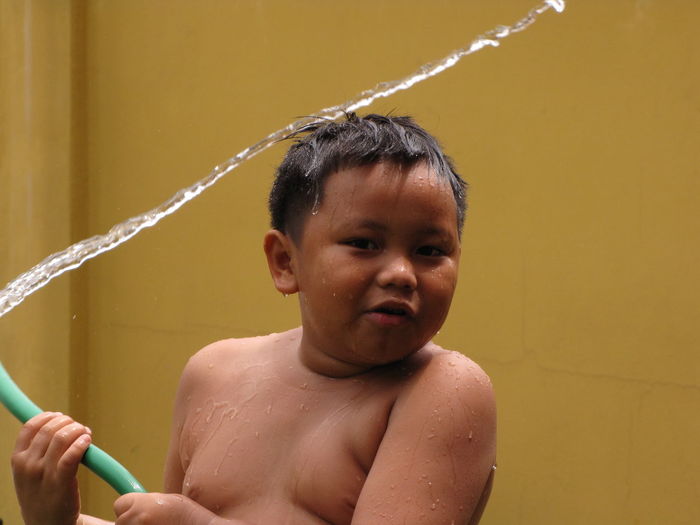 Portrait of boy splashing water against wall