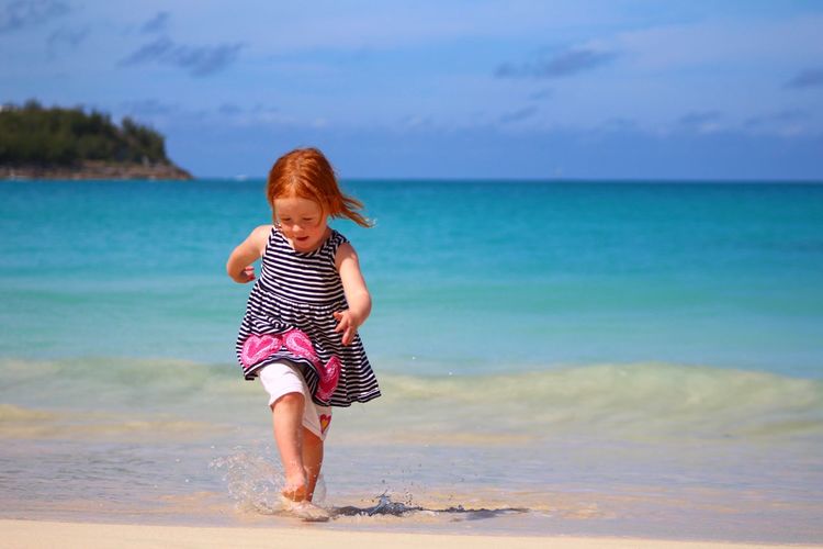 Girl running on sea shore at beach against sky