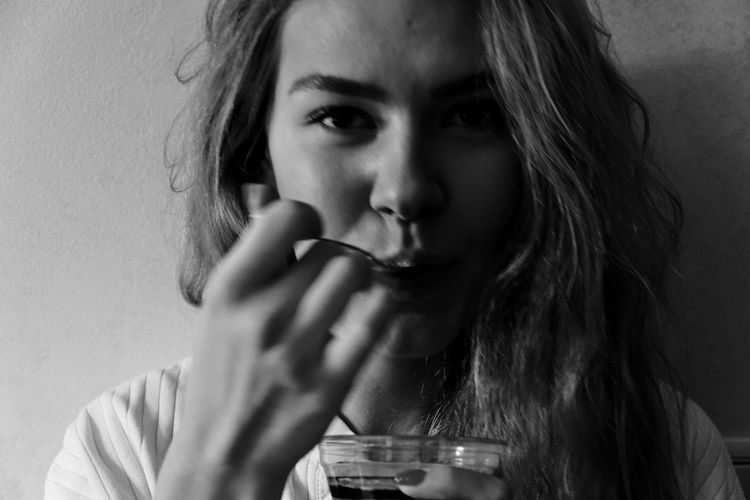 Close-up portrait of young woman drinking glass against wall