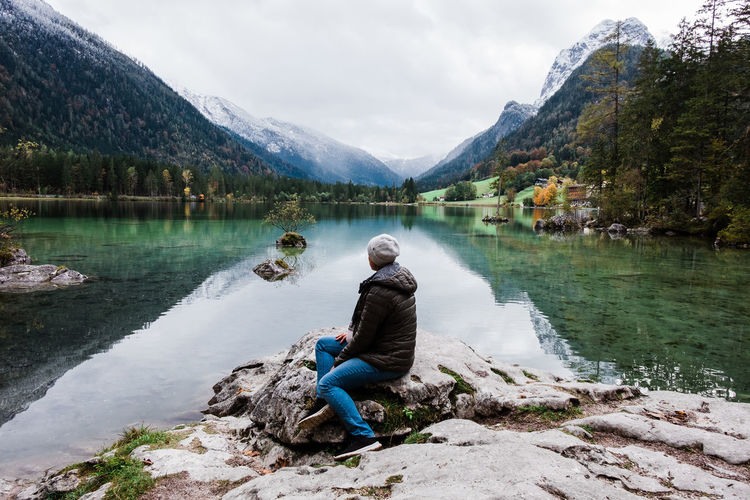 Full length of woman sitting on rock by lake against sky