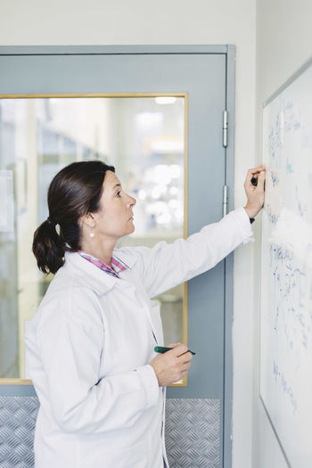 Female scientist analyzing plan on whiteboard at laboratory