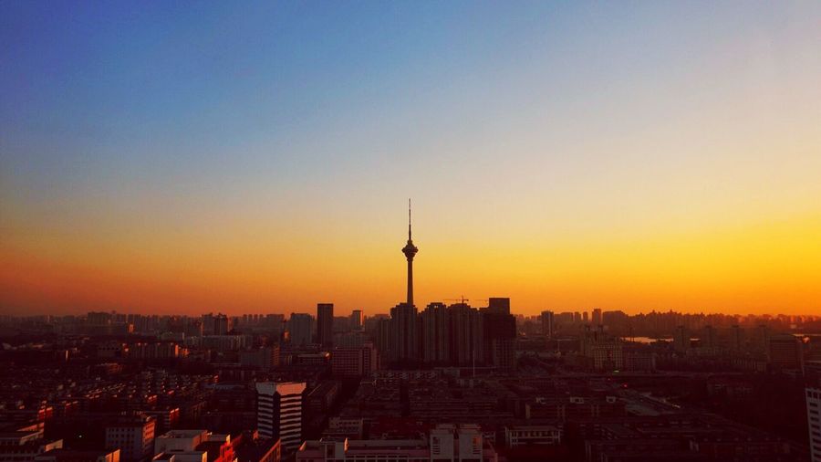 Silhouette tianjin radio and television tower in city against orange sky