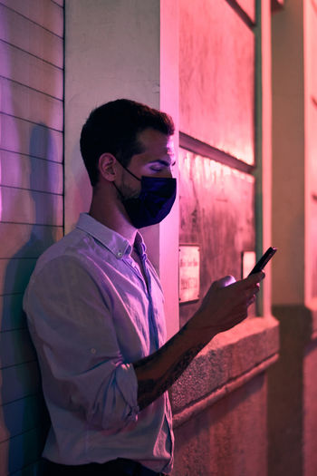 Portrait of young man using mobile phone against wall