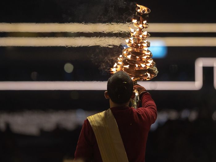 Rear view of hindu priest praying river at night
