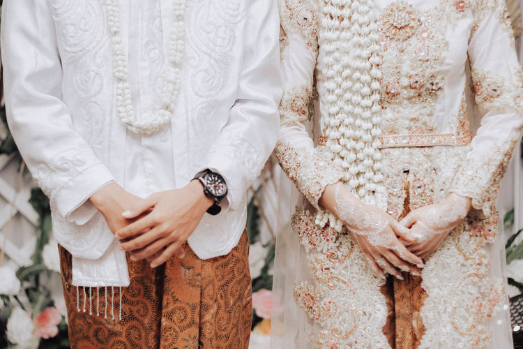 MIDSECTION OF COUPLE HOLDING HANDS STANDING BY WHITE