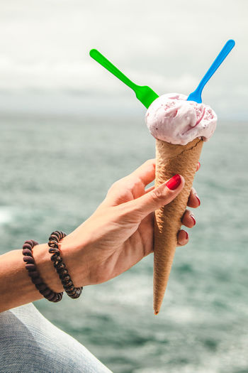 Cropped hand of woman holding ice cream cone against sea