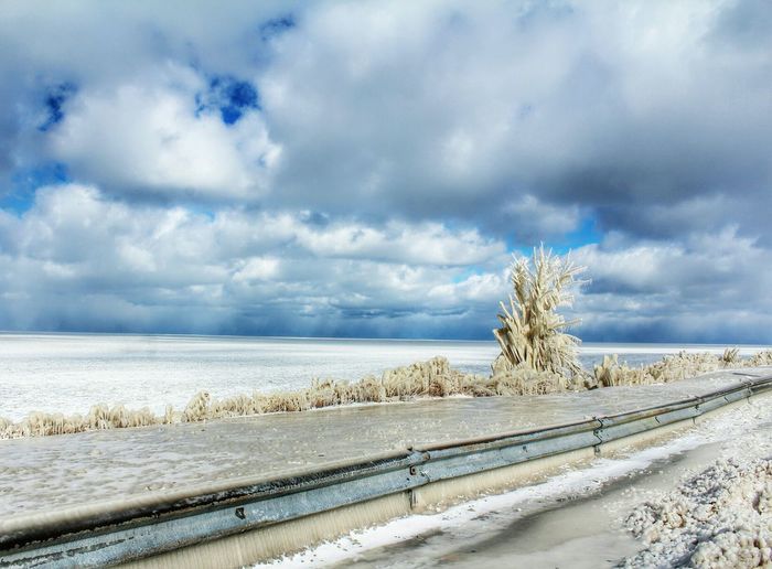 Scenic view of frozen lake erie against cloudy sky on sunny day