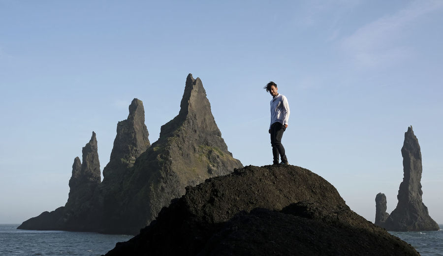 Man standing on rock at black beach, iceland, with wind in his hair