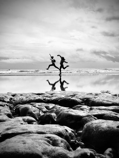 Friends jumping at beach against cloudy sky