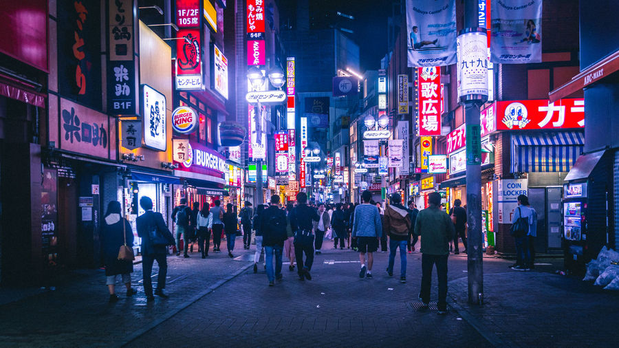 People walking on street amidst illuminated buildings in city at night