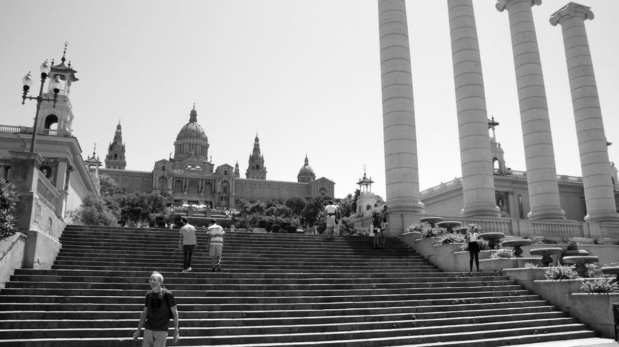 People walking on steps by museu nacional d art de catalunya against clear sky