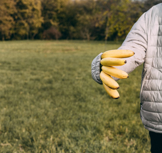 Midsection of man holding banana while standing on field