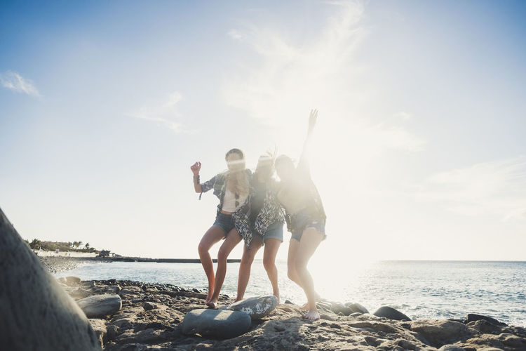 Friends standing at beach against sky