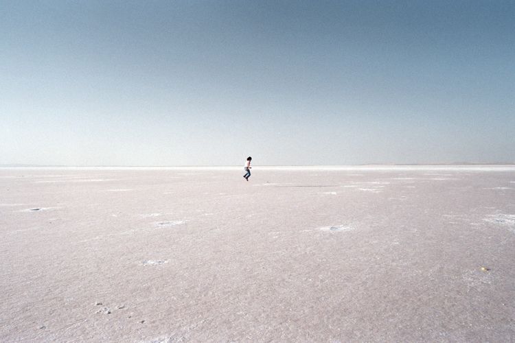 Distant view of person jumping on field against clear sky