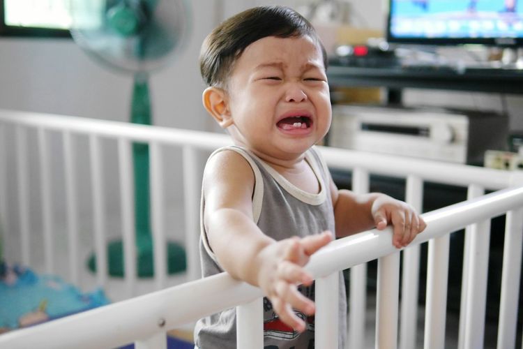 Close-up of baby boy crying in crib at home