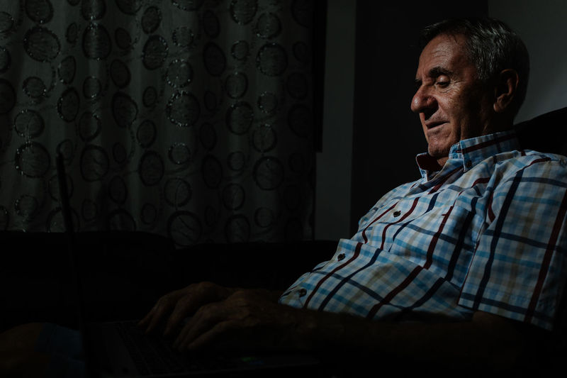 Senior man browsing laptop in dark room
