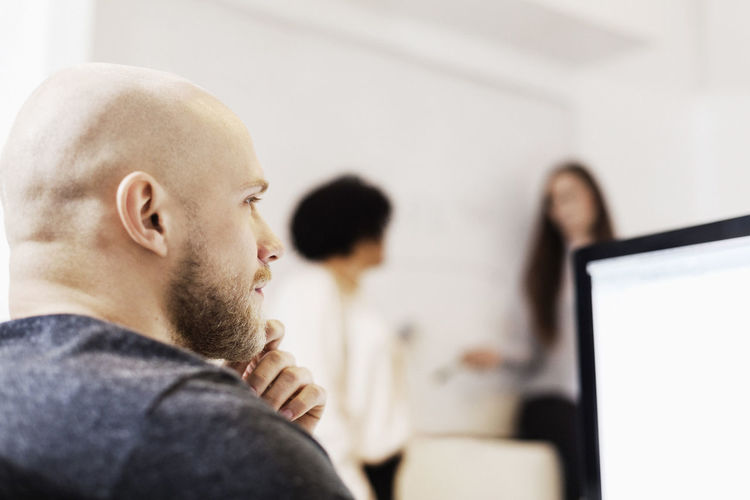 Thoughtful businessman looking away while colleagues discussing in background at office