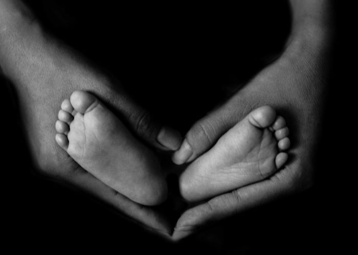 Cropped hands of parent holding child feet against black background