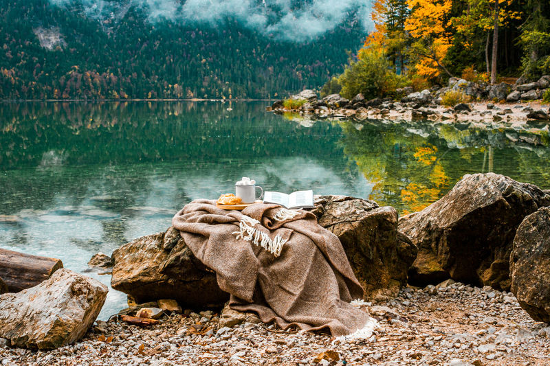 Picnic with cacao on stones near lake and autumn forest in the bavarian mountains, germany