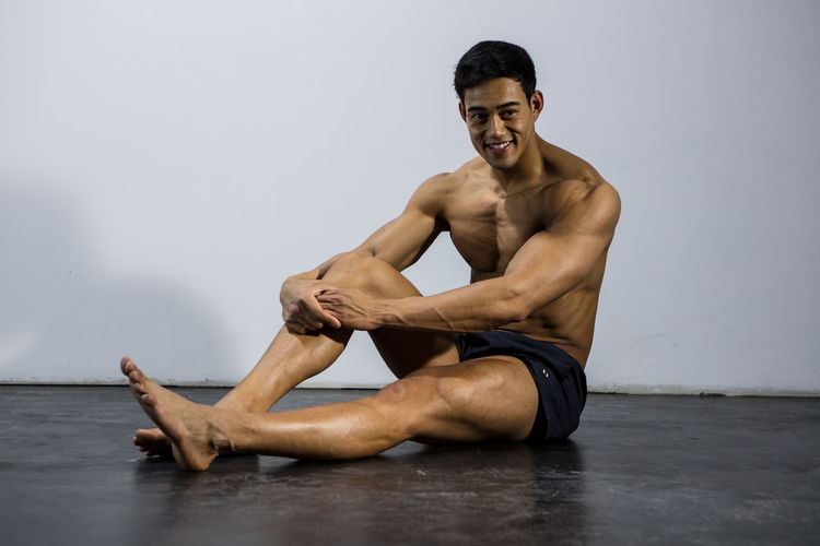 Portrait of shirtless muscular man sitting against wall