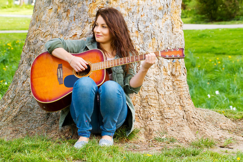 Full length of young woman playing guitar by tree at park