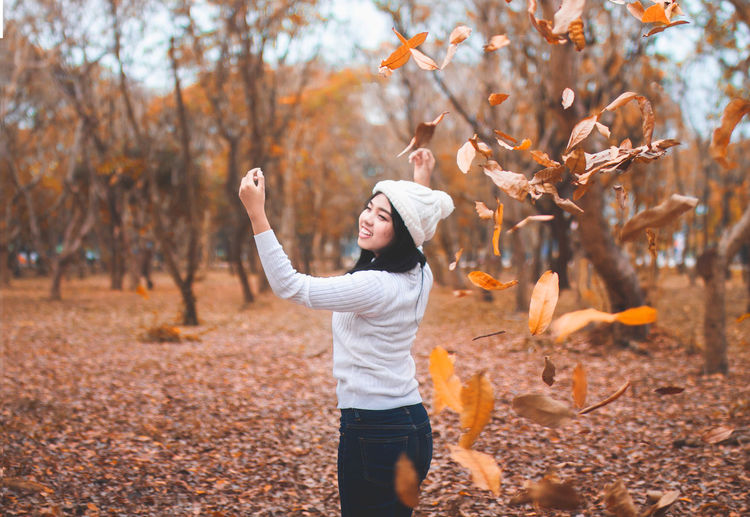 Happy young woman playing with leaves in park during autumn