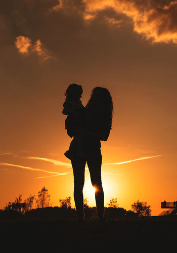 Silhouette couple standing against orange sky