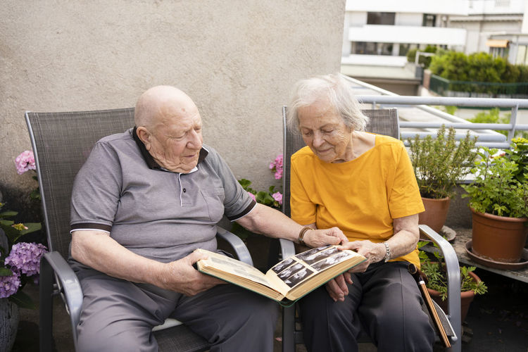 Senior man with woman looking at photo album sitting on balcony