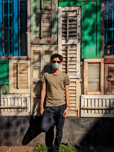 Full length of young man  in mask standing against a decorated wall