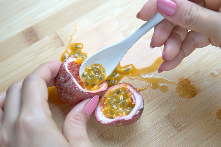 High angle view of woman hands holding passion fruit and spoon on table